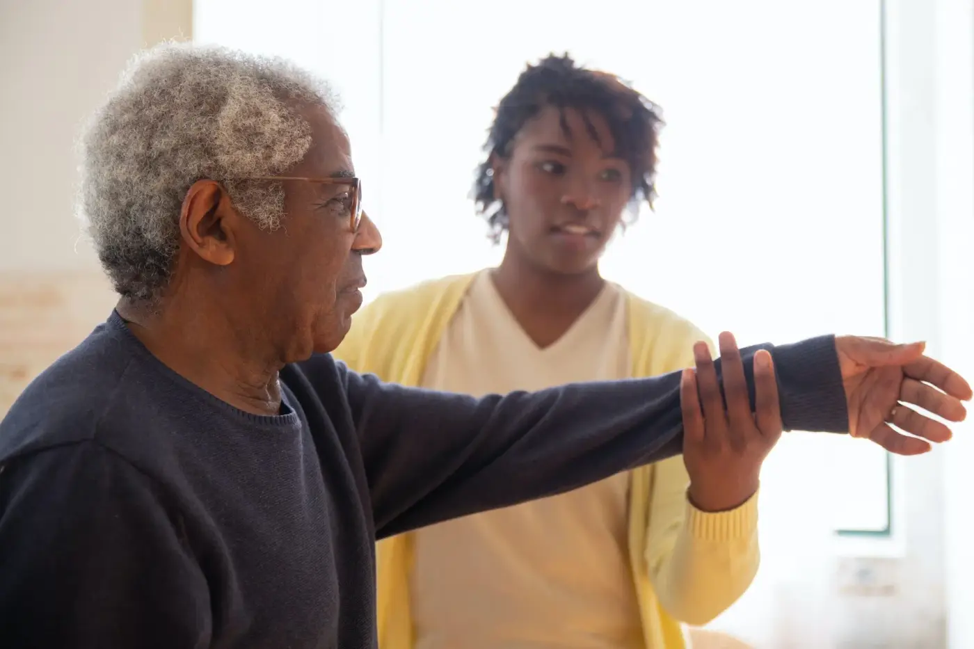 lady in a yellow cardigan helping elderly man